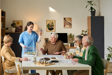 Senior group playing game with female caregiver in care home, engaging in cognitive activity and...