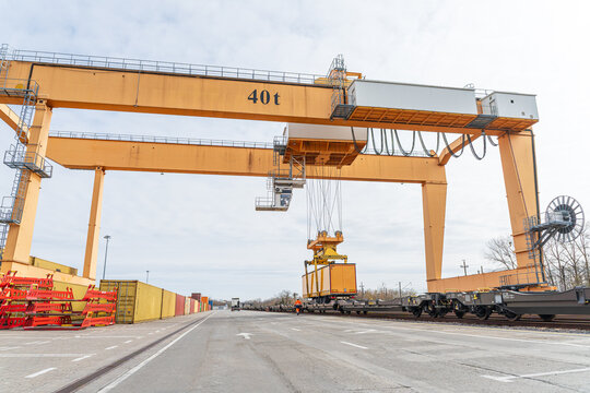 Large gantry crane operating at an intermodal logistics terminal, loading a semi-trailer onto a freight train for sustainable combined rail and road transportation