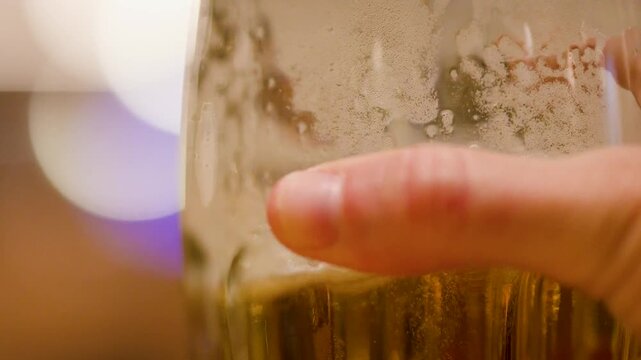 Close up video of human hand holding and then putting down a glass of frothy beer.