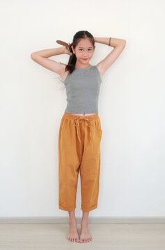 Portrait of young Asian girl brushing her hair while standing in white room with smiling at the camera.