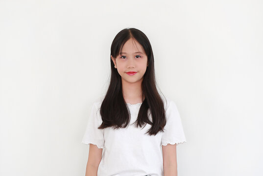 Portrait of charming young Asian girl with long, dark hair and light makeup, wearing a simple white t-shirt while posing with gentle smile against white background.