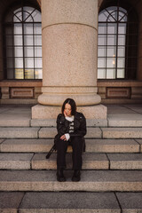 Naklejka premium Stylish woman in leather jacket sitting on stone steps in city