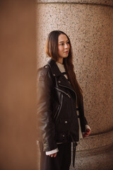 Naklejka premium Stylish woman in leather jacket standing by stone column in city
