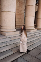 Naklejka premium Elegant woman in trench coat walking by stone columns in city