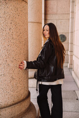 Naklejka premium Stylish woman in leather jacket standing by stone column in city