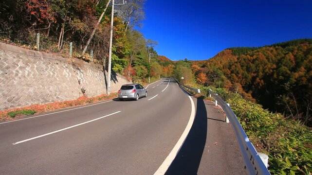 鳥居峠付近の国道144号と自動車と太陽の光芒と樹林