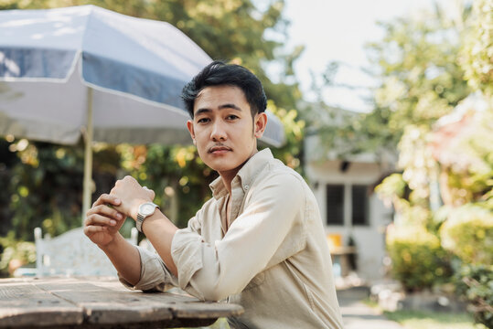 A pensive young Asian man posing calmly at table. Outdoor shot.