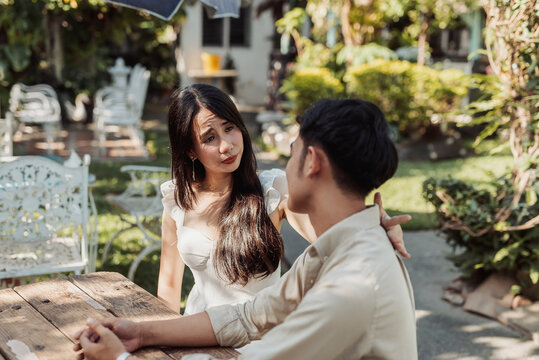 A caring and empathetic young Asian woman gently listening while her boyfriend opens up about his feelings during an emotional relationship conversation. Outdoor shot.