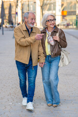 Fototapeta premium Smiling senior couple holding hands walking city street