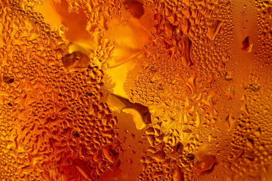 A close-up image of a cold cola with condensation on a glass background,Macro shot of a refreshing amber-colored drink with ice cubes, showing heavy water condensation droplets on the outside.