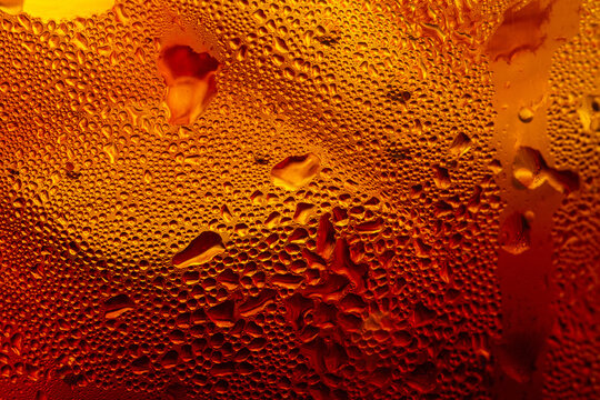 A close-up image of a cold cola with condensation on a glass background,Macro shot of a refreshing amber-colored drink with ice cubes, showing heavy water condensation droplets on the outside.