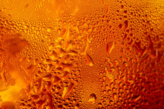 A close-up image of a cold cola with condensation on a glass background,Macro shot of a refreshing amber-colored drink with ice cubes, showing heavy water condensation droplets on the outside.