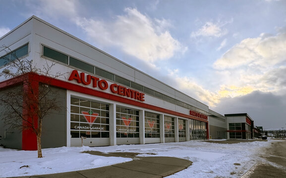 Calgary, Alberta, Canada. April 14, 2026. External view of a Canadian Tire Auto Centre building with snow on the ground under a cloudy sky.