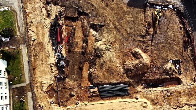 Excavation site with trenches and pipes, preparing for ground utility installation, aerial top down view