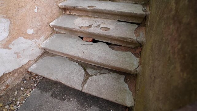 Damaged concrete staircase with cracked steps and deep gaps beside an old plaster wall, showing unsafe access, neglect, and hazardous building deterioration.