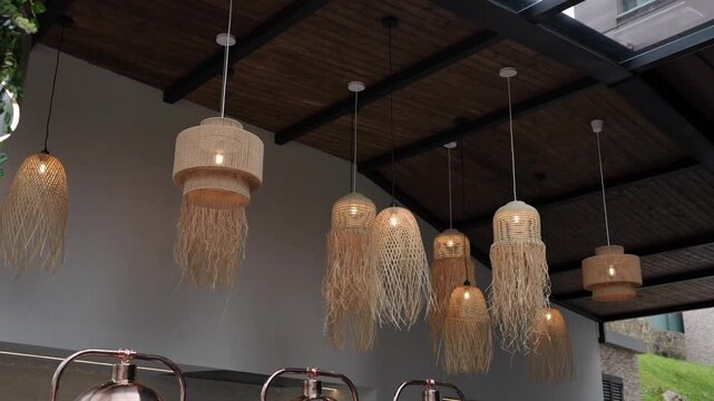 Multiple woven rattan and raffia fringe pendant lights suspended from a dark wooden beam ceiling, copper vessels visible below