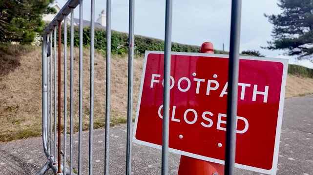 Red footpath closed sign behind a metal railing along a walkway, signaling restriction and safety.