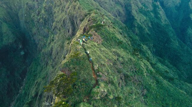 High-angle shot of a narrow ridge path with people walking through a rugged green landscape.