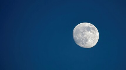 Obraz premium Bright full moon with clear craters and maria details visible against deep blue daytime sky, solitary and serene in mini