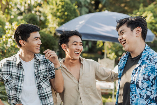 A joyful young Asian college friends laughing together while bonding and sharing fun moments during a sunny day outdoors. Outdoor shot.
