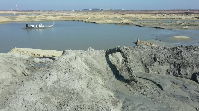 Mixture water and sand flow from big pipe, pump discharge for sand sedimentation. Water flows and carries sand from opencast surface mining, excavating sand and his deposition.