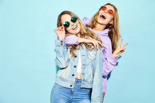 Two young beautiful blond smiling hipster in trendy summer clothes. Sexy carefree women posing near blue wall in sunglasses. Positive models going crazy