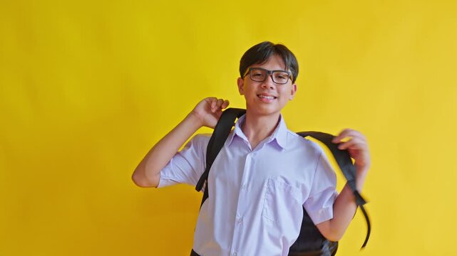 Happy junior high school student in school uniform putting on backpack against yellow background