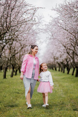 Fototapeta premium Mother and daughter walking in blooming almond spring orchard.