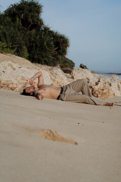 Shirtless man lying on beach full length with rocks and jungle