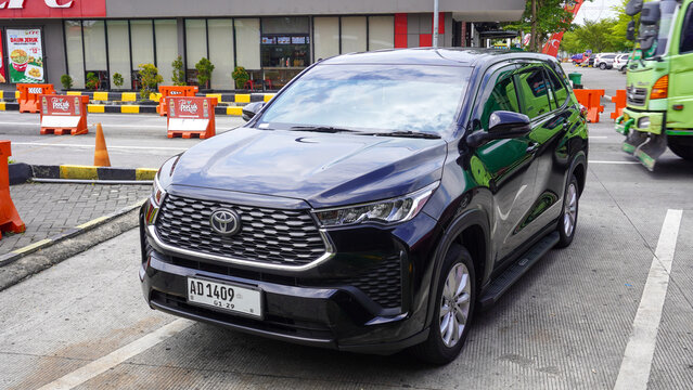 Modern black Toyota Kijang Innova Zenix MPV parked at a rest area in Indonesia, showcasing its sleek front grill design, LED headlights, dark body paint, dynamic vehicle stance, and city street.