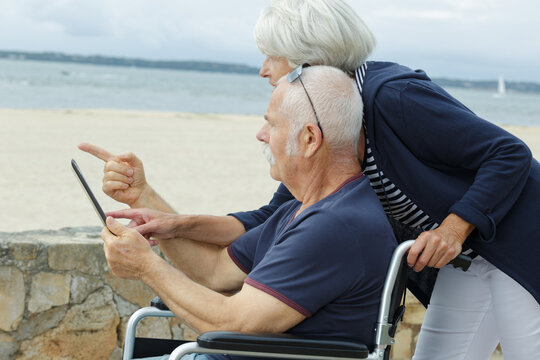senior couple by the beach with tablet man in wheelchair