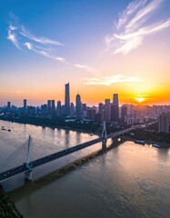 Fototapeta premium A stunning aerial view captures a modern cityscape bathed in the warm hues of a vibrant sunset, with a graceful cable-stayed bridge spanning a wide river.