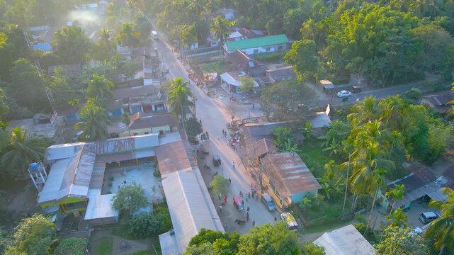 Drone view of road with shops, school buildings, people, and vehicles in Byaskuchi village, Assam.