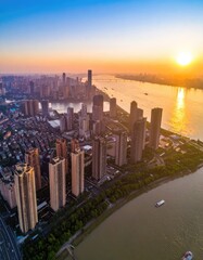 Fototapeta premium An aerial view captures a sprawling cityscape bathed in the warm hues of a setting sun, showcasing a modern metropolis nestled along a wide river.