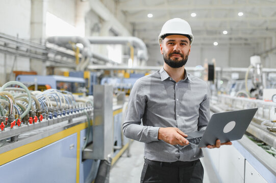 Industrial engineer holding laptop, managing production line in factory