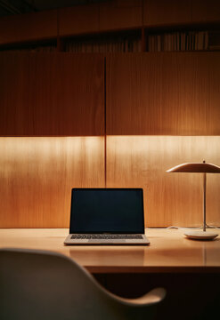 Open Laptop on Wooden Desk with Warm LED Backlit Shelving in Cozy Dark Office Interior