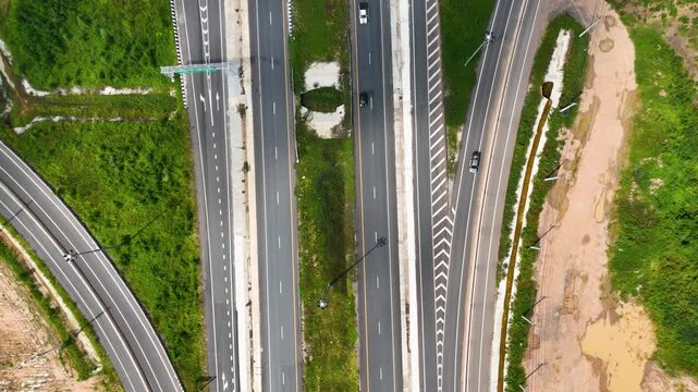 4K UHD Top down aerial view of rural highway with light traffic. Clean road infrastructure surrounded by greenery for transport, travel, and development concepts