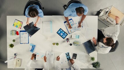 Top down view of doctors participating in a healthcare team meeting to review patient care. The discussion focuses on treatment planning and advancement in modern medicine. © DC Studio