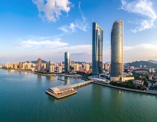Obraz premium An aerial view showcases the modern skyline of a coastal Chinese city, featuring towering skyscrapers reflected in the calm waters of a bay under a clear blue sky.