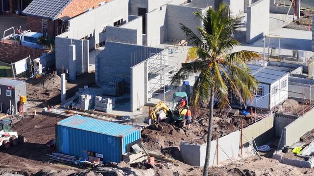 Aerial view of construction site with workers and excavating machinery building new concrete block houses.