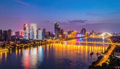 Fototapeta premium A stunning panoramic view of a modern cityscape at dusk, showcasing illuminated skyscrapers reflected in a wide river with a graceful arch bridge spanning across.