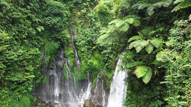 Beautiful waterfall flowing down a rocky cliff covered in dense tropical rainforest vegetation.