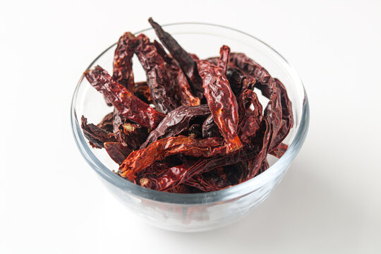 A glass bowl of long, wrinkled dried red chili peppers, commonly used as a base for spicy condiments and seasonings.