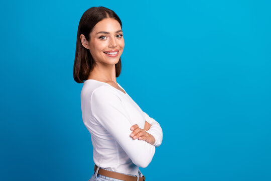 Young woman smiling in white shirt stands with arms crossed against a blue studio background