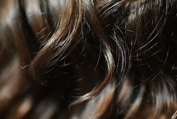 Naklejka premium Subject: Brown hair. Action: Close-up of textured, wavy hair strands. Setting: Dark background.