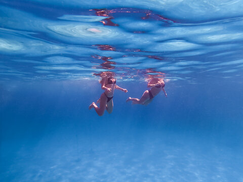 Two women swimming underwater in the crystal clear turquoise water of the Red Sea in Egypt during summer vacation