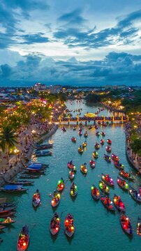 Traditional wooden boats carrying men and women with colorful lanterns during an aerial hyperlapse sequence on the river at dusk in Hoi An, Vietnam.