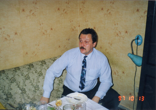 Man in light blue shirt and tie leaning on table with plates and glass in domestic interior, analog color film print dated October 1997