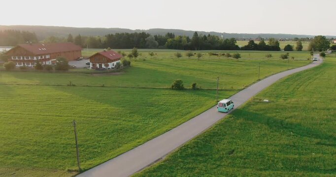 Title:
Aerial view of small van driving on narrow road through green meadow and rural countryside landscape
