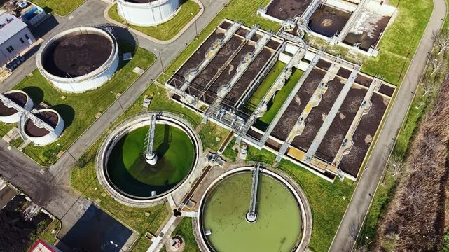 Workers manage various tanks and equipment that treat wastewater. The facility includes circular tanks, pipes, and green areas. This site helps clean water for the city.